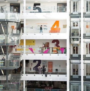 Innenansicht eines modernen Hochschulgebäudes mit mehreren Etagen und Studierenden auf den Fluren.