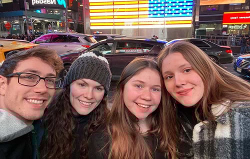 Vier Personen lächeln mit Autos im Hintergrund