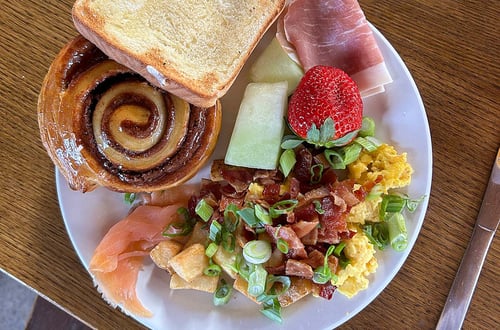 Essenteller mit Zimtschnecke, Toast, Obst, Ei und Speck