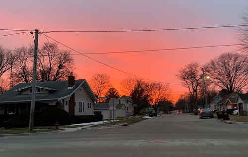 Von der Straße aus fotografierter roter Himmel mit Häusern und Bäumen entlang der Straße