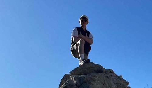 Ein Junge posiert auf einem Stein und blauem Himmel im Hintergrund