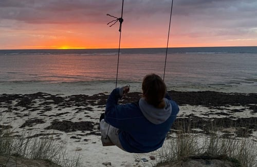 Eine Person schaukelt am Meer bei Sonnenuntergang
