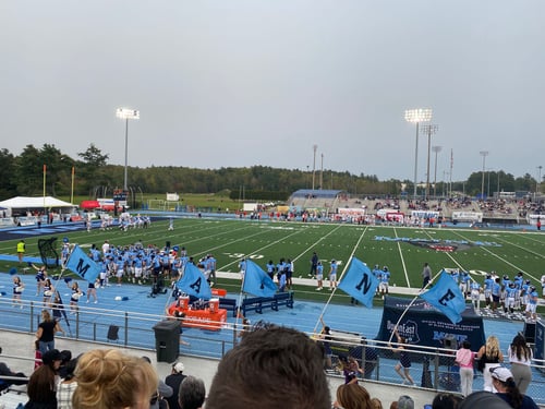 Ein Football Feld mit Spielern am Rand in blauen Trickots