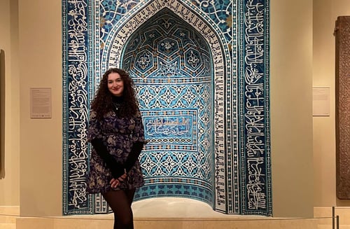 Ein Mädchen posiert vor einem von Mustern und arabischen Schriftzeichen verziertem Museumsstück