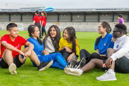 Eine Gruppe Schülerinnen und Schüler sitzt auf der Wiese vor einem Gebäude auf dem Campus des Abbey College.