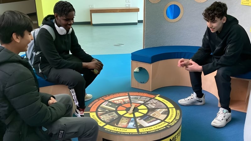 Schüler des Abbey College Manchester versammeln sich um ein großes rundes Spielbrett auf dem Boden für eine kooperative Aktivität.