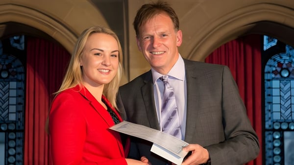 Ein Mann und eine Frau in formeller Kleidung stehen vor bunten Glasfenstern auf dem Campus des Abbey College Manchester.