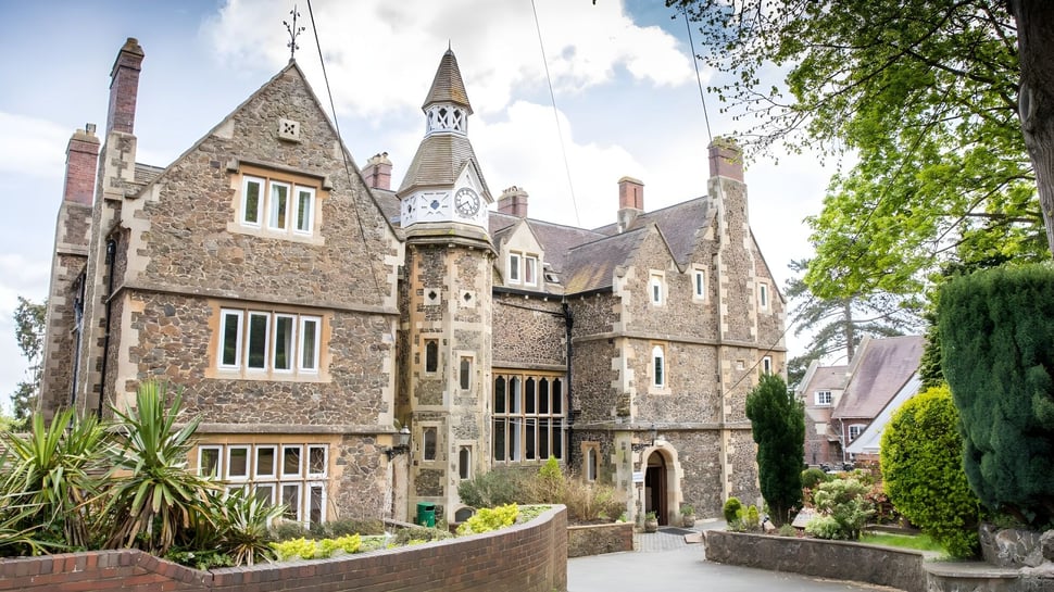 Das mittelalterliche Schloss mit aufwendiger Architektur auf dem Gelände des Abbey College ist von grüner Vegetation umgeben.