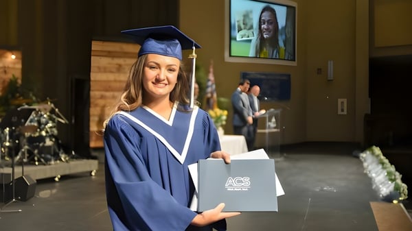 Eine junge Frau in Abschlusskleidung hält ihr Diplom auf dem Campus der Abbotsford Christian School.