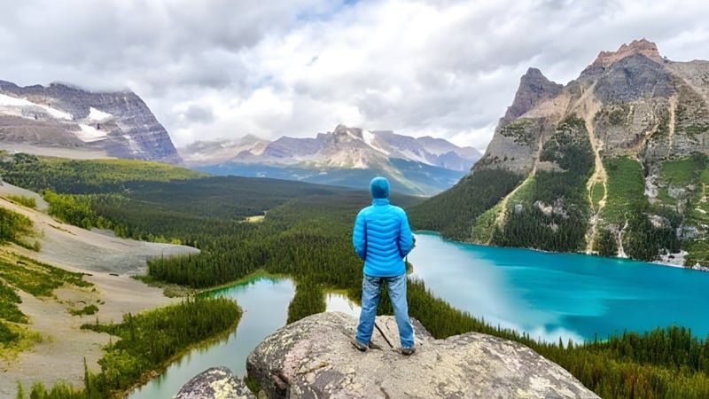 Eine Person in blauem Outfit steht auf einem Felsen mit Blick auf die Berglandschaft und den See nahe der Abbotsford Senior Secondary School.