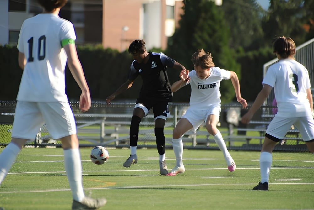 Eine Gruppe Schüler spielt Fußball auf dem grünen Feld der Abbotsford Senior Secondary School mit Gebäuden und Bäumen im Hintergrund.