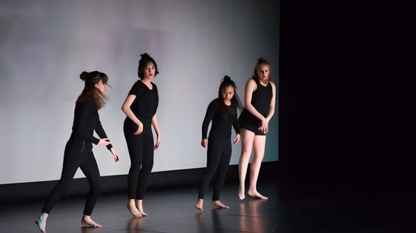 Vier Personen stehen in schwarzer Kleidung vor schlichtem Hintergrund auf dem Campus der Abbotsford Senior Secondary School.