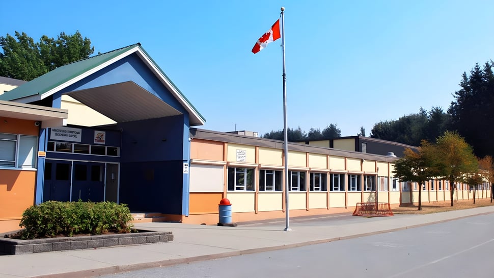 Das moderne mehrstöckige Gebäude der Abbotsford Traditional Secondary School mit einer kanadischen Flagge auf dem Dach und Bäumen im Vordergrund.