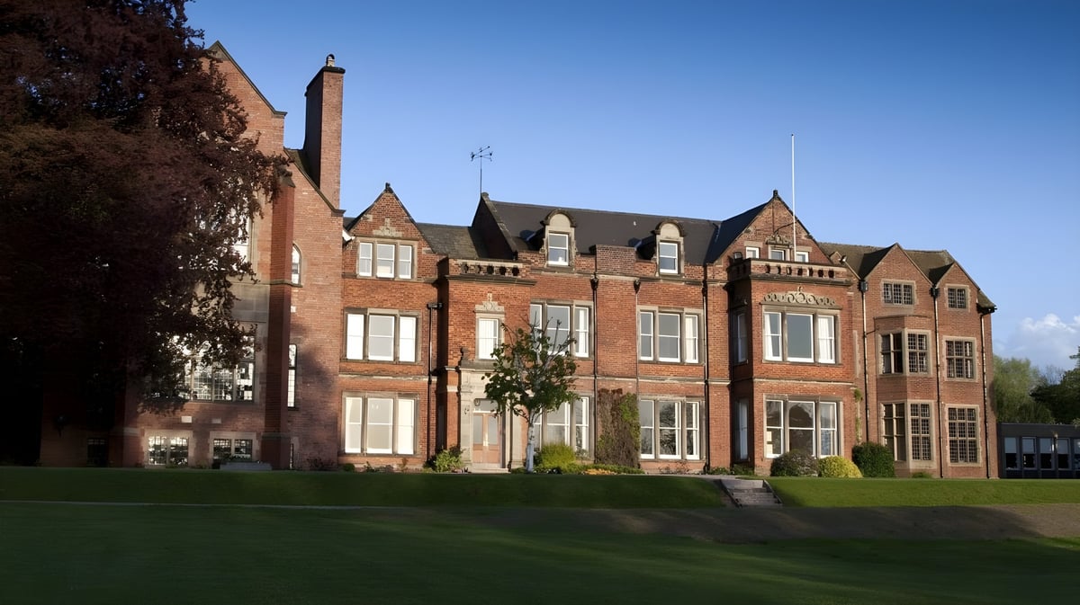 Das historische Backsteingebäude der Abbotsholme School steht auf einer Grasfläche unter klarem blauem Himmel.