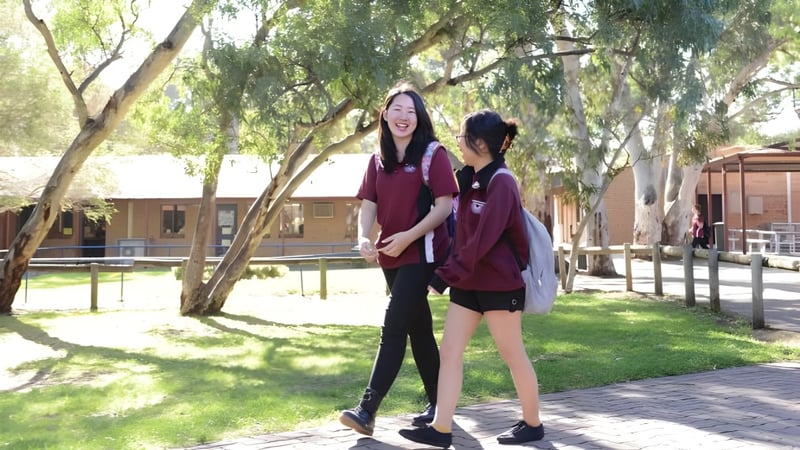 Zwei Schülerinnen der Aberfoyle Park High School stehen gemeinsam in einer parkähnlichen Umgebung mit viel Grün und Bäumen.