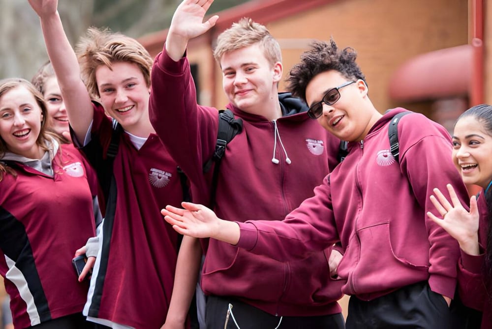 Eine Gruppe von Schülerinnen und Schülern der Aberfoyle Park High School steht zusammen vor einer roten Backsteinwand im Freien.