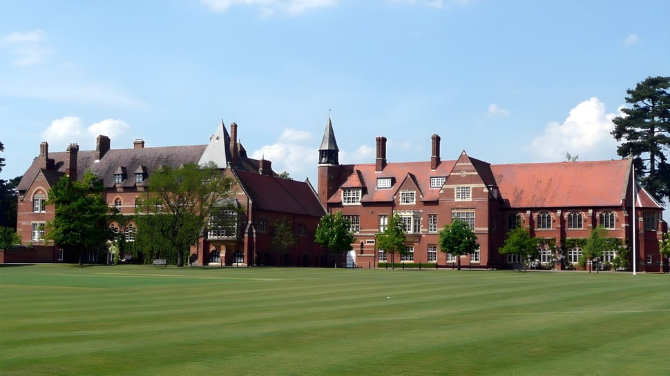 Das historische Backsteingebäude der Abingdon School steht hinter einem gepflegten grünen Rasen unter blauem Himmel.