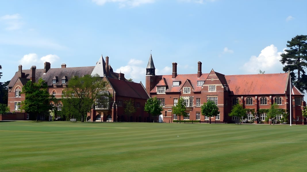 Das historische Backsteingebäude der Abingdon School steht hinter einem gepflegten grünen Rasen unter blauem Himmel.