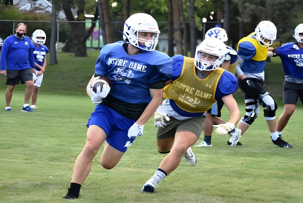 Eine Gruppe von Fußballspielern der Academy of Notre Dame trainiert auf einem Spielfeld mit Bäumen und Gebäuden im Hintergrund.