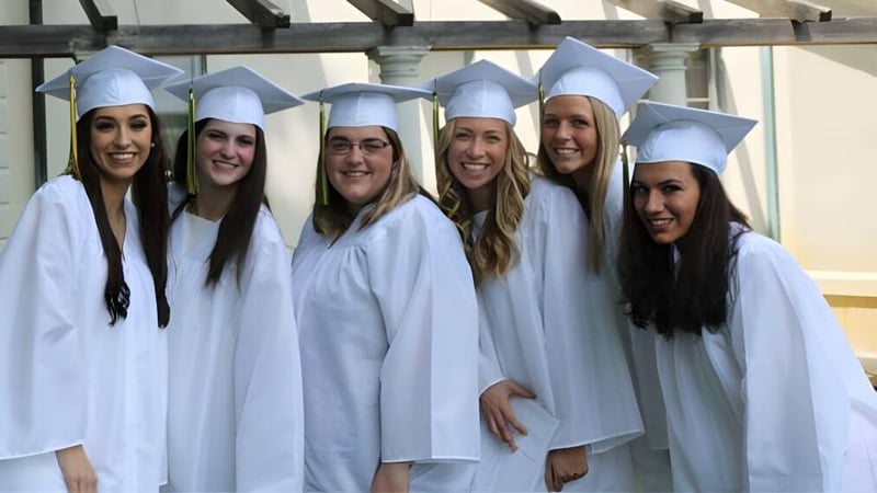 Eine Gruppe junger Frauen in weißen Abschlusskleidern steht im Schulgebäude der Academy of Notre Dame.