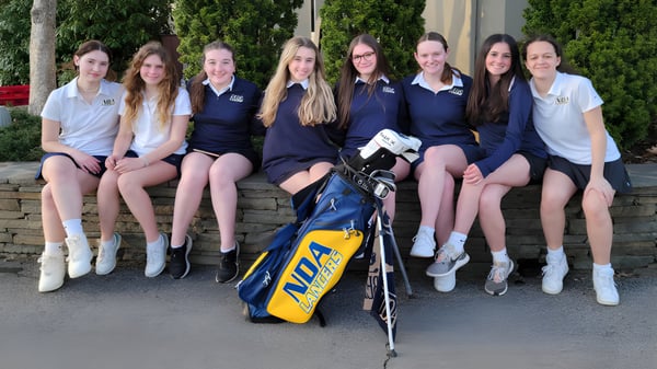 Schülerinnen der Academy of Notre Dame sitzen zusammen auf einer Mauer mit einer Golf-Tasche im Vordergrund.