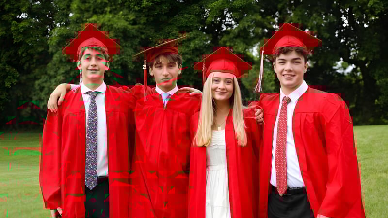 Vier Schüler der Academy of the New Church tragen rote Abschlussroben und Hüte und stehen zusammen auf einer Wiese mit Bäumen im Hintergrund.