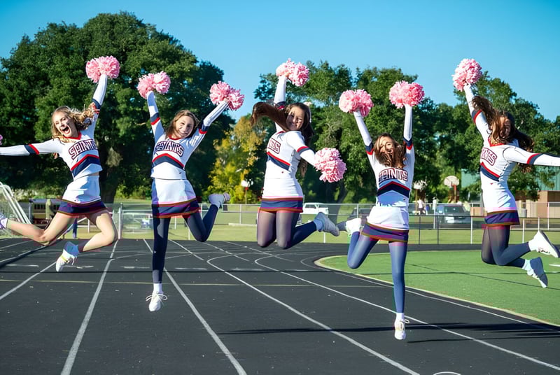 Schülerinnen der Academy of the Sacred Heart führen auf dem Sportfeld eine Cheerleader-Performance vor grüner Umgebung und blauem Himmel auf.