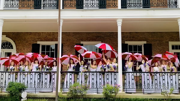 Eine Gruppe von Schülerinnen und Schülern mit bunten Regenschirmen steht auf dem Balkon eines Backsteingebäudes der Academy of the Sacred Heart.