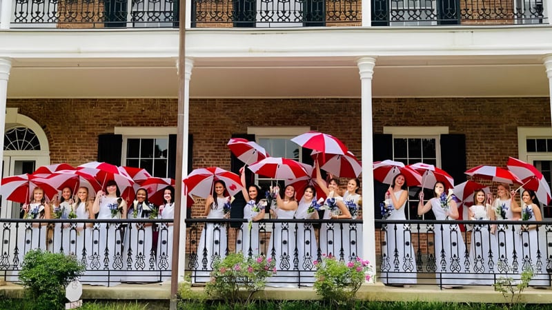 Eine Gruppe von Schülerinnen und Schülern mit bunten Regenschirmen steht auf dem Balkon eines Backsteingebäudes der Academy of the Sacred Heart.