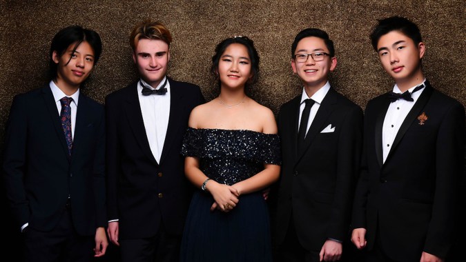 Fünf formal gekleidete Schülerinnen und Schüler stehen vor dunklem Hintergrund auf dem Campus des ACG Parnell College.