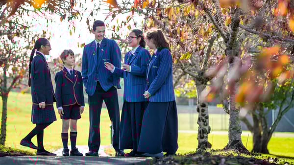 Eine Gruppe Schüler in Schuluniformen steht auf dem Campus der ACG Sunderland vor herbstlicher Bepflanzung.