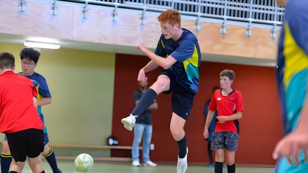 Ein Schüler der ACG Tauranga spielt Fußball in der Sporthalle, umgeben von weiteren Schülern.