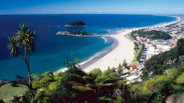 Eine Küstenlandschaft mit Halbmondstrand und türkisfarbenem Wasser vor der Kulisse von Bergen, die an der ACG Tauranga liegt.