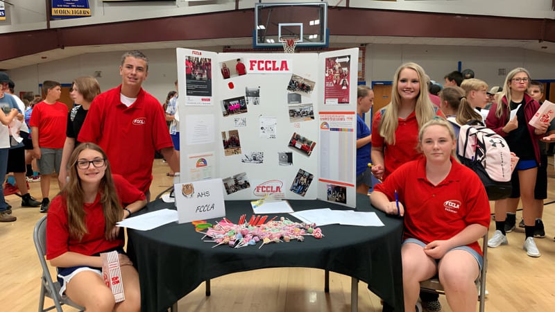 Eine Gruppe Schülerinnen und Schüler der Acorn High School steht in der Turnhalle um einen Präsentationstisch mit Postern und Materialien.