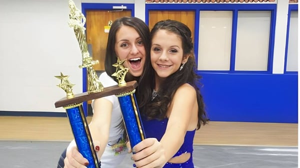 Zwei Schülerinnen der Acorn High School halten lächelnd einen Pokal in einem Raum mit blauen Wänden.