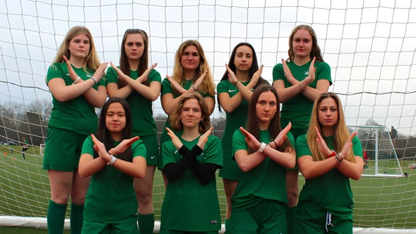 Eine Gruppe von Schülerinnen in grünen Uniformen steht vor dem Fußballtor auf dem Sportplatz der ACS International School Cobham.