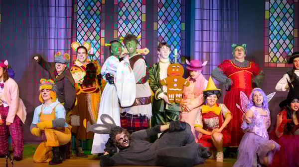 Schüler der ACS International School Cobham führen eine bunte Theateraufführung vor einem Kirchenfenster-Hintergrund auf.