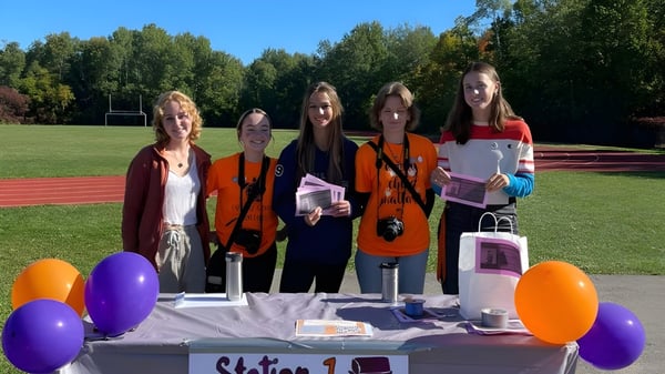 Eine Gruppe Schülerinnen der Acton High School steht auf einem Rasenfeld vor Bäumen zwischen bunten Luftballons und Dekorationen.