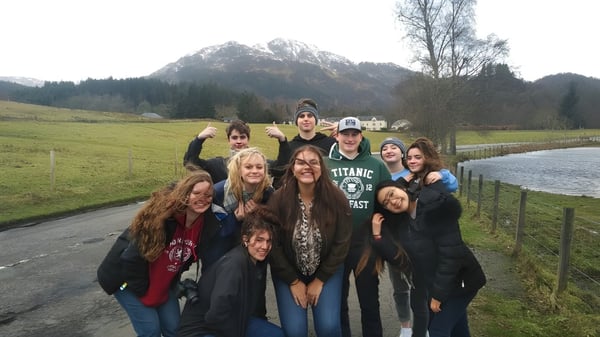 Eine Gruppe von Schülern der Acton High School steht gemeinsam in einer landschaftlich reizvollen Außenanlage mit Bergen und Bäumen im Hintergrund.