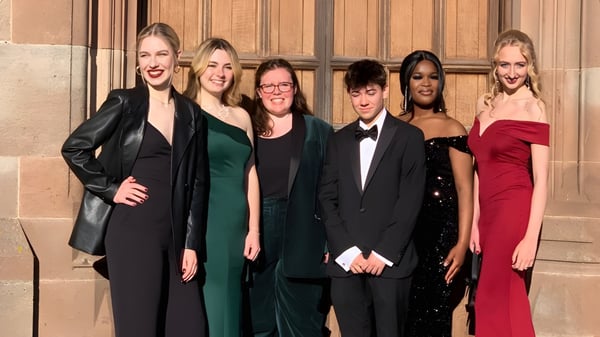 Eine Gruppe von Personen steht vor einer Holzstruktur auf dem Gelände der Adcote School.
