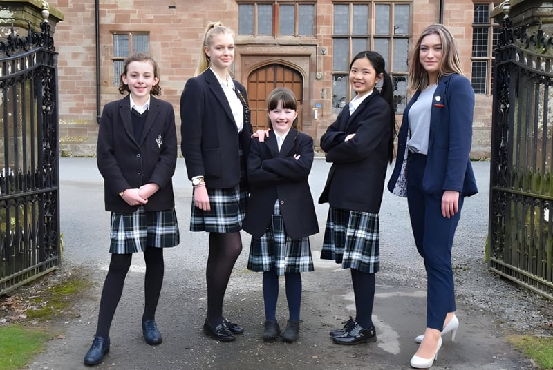 Eine Gruppe Schülerinnen der Adcote School steht vor einem Backsteingebäude mit verzierten Toren.