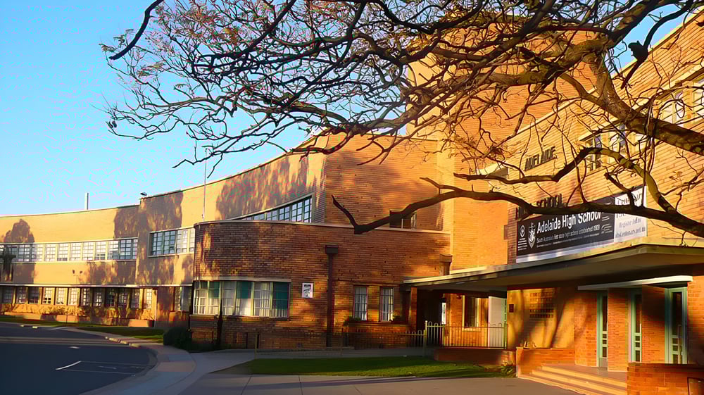 Das Backsteingebäude der Adelaide High School mit Balkon ist von kahlen Bäumen vor klarem, blauem Himmel bei warmem Sonnenlicht umgeben.
