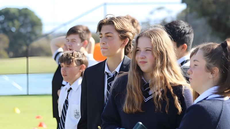 Eine Gruppe von Schülerinnen und Schülern der Adelaide High School steht auf einem Grasfeld neben Schulgebäuden und Bäumen.