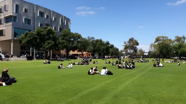 Viele Schüler sitzen auf einer grünen Wiese vor dem mehrstöckigen Gebäude der Adelaide High School.