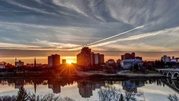 Ein beeindruckendes Stadtbild mit Hochhäusern spiegelt sich im ruhigen Fluss unter einem farbenfrohen Sonnenuntergang bei der Aden Bowman Collegiate.