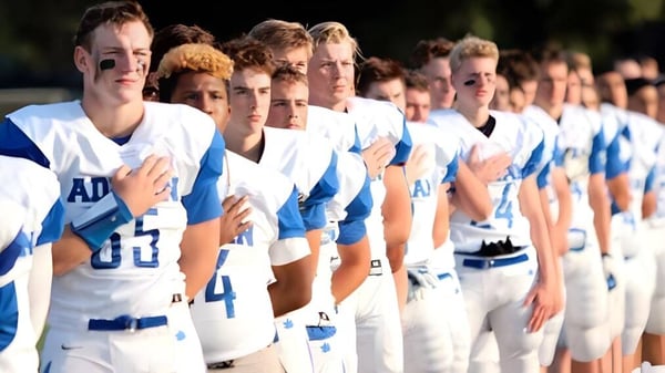 Eine Gruppe junger Athleten steht in weißen und blauen Uniformen in einer Reihe auf dem Sportfeld der Adrian High School.