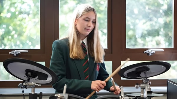 Eine Schülerin der Akeley Wood School spielt Schlagzeug in einem gemütlichen Innenraum mit Fenster im Hintergrund.