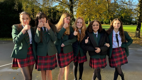 Eine Gruppe Schülerinnen der Akeley Wood School steht im Schuluniform zusammen in einem Park mit Bäumen und Pflanzen.