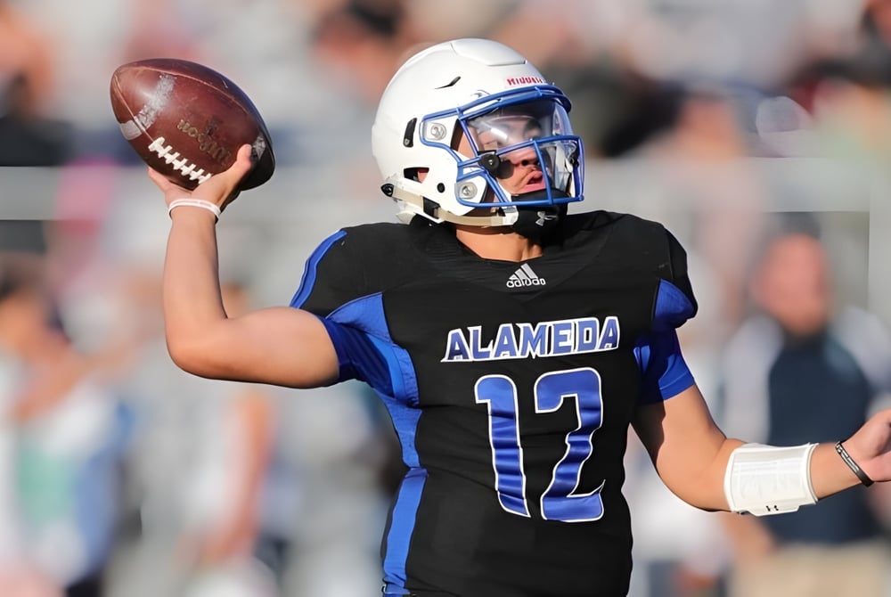 Ein Footballspieler im schwarzen und blauen Trikot hält den Football auf dem Spielfeld des Alameda Unified School District.