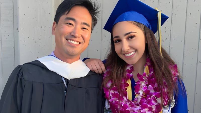 Zwei Absolventen in Talaren und Hüten posieren gemeinsam vor einer Holzwand auf dem Campus des Alameda Unified School District.